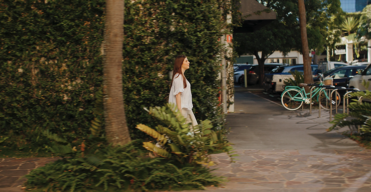woman walking outside of greenery covered precinct